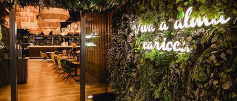 An indoor space with a wooden floor, a bar area, and a neon sign that reads "Viva a vida caricia."