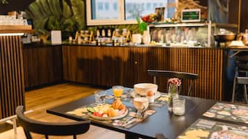 Een ontbijt met croissants, eieren en fruit, een glas sinaasappelsap en een vaas met bloemen op een tafel.