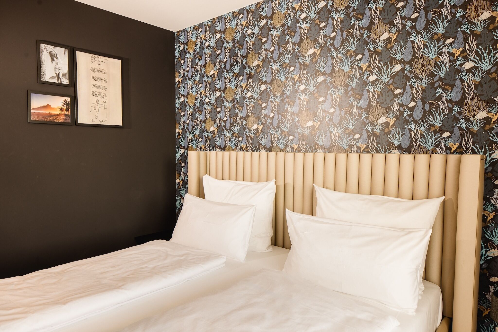 A hotel room with a bed, a headboard, and a wall with a leaf pattern.