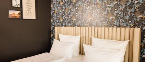 A hotel room with a bed, a headboard, and a wall with a leaf pattern.