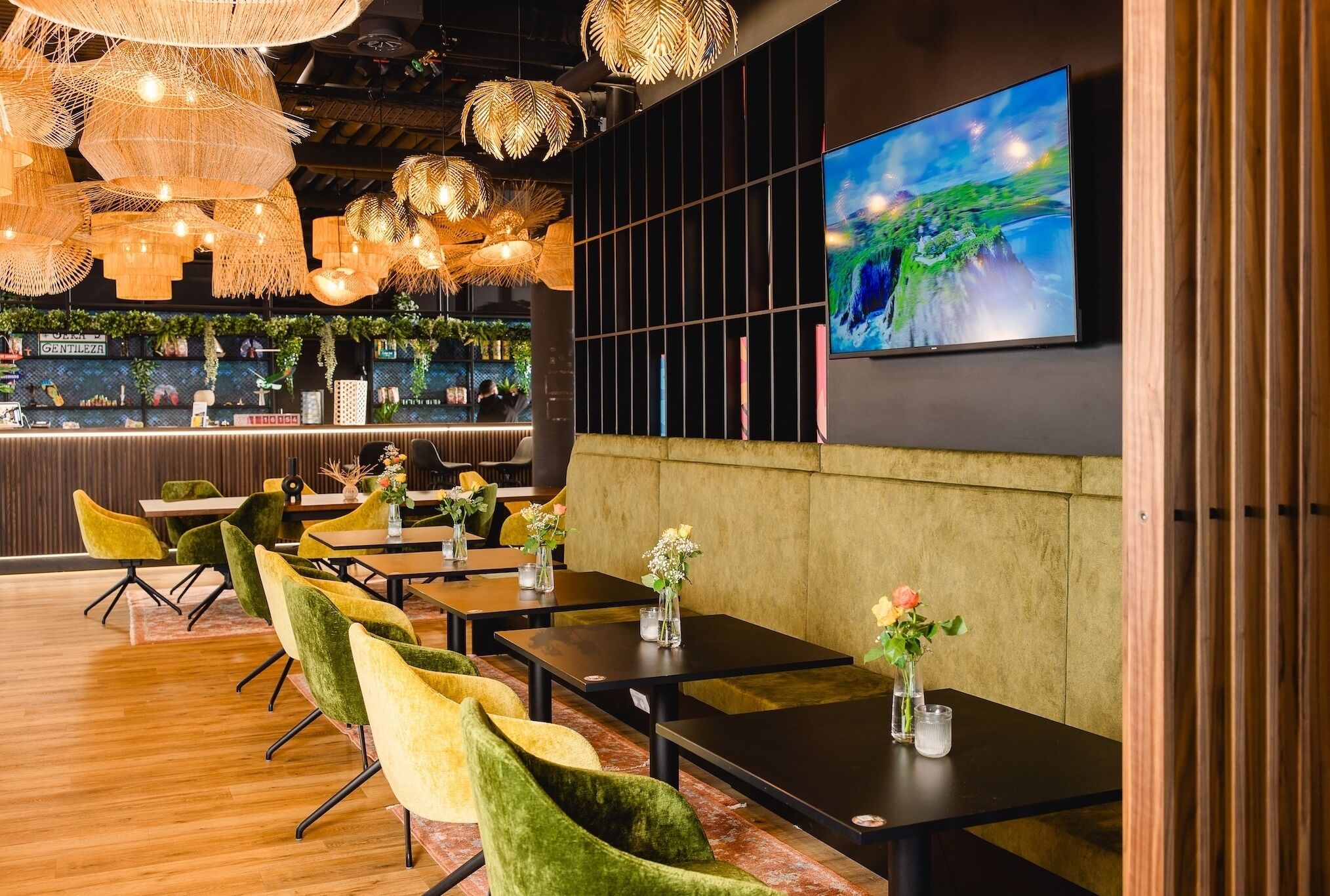 Un restaurante con mesas de madera, sillas de terciopelo verde y lámparas de mimbre colgantes.