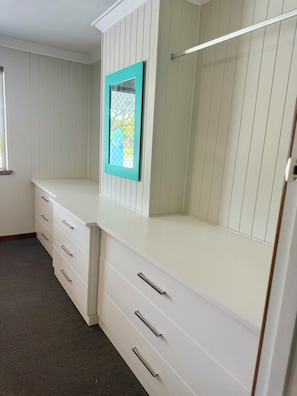 A room with a white wardrobe, a window with a turquoise frame, and a carpeted floor.