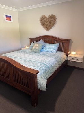 A bedroom with a wooden bed, patterned bedding, a heart-shaped wall decoration, and bedside lamps.