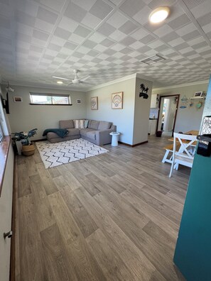 A spacious living area with a large sectional sofa, a herringbone-patterned rug, and a ceiling fan.