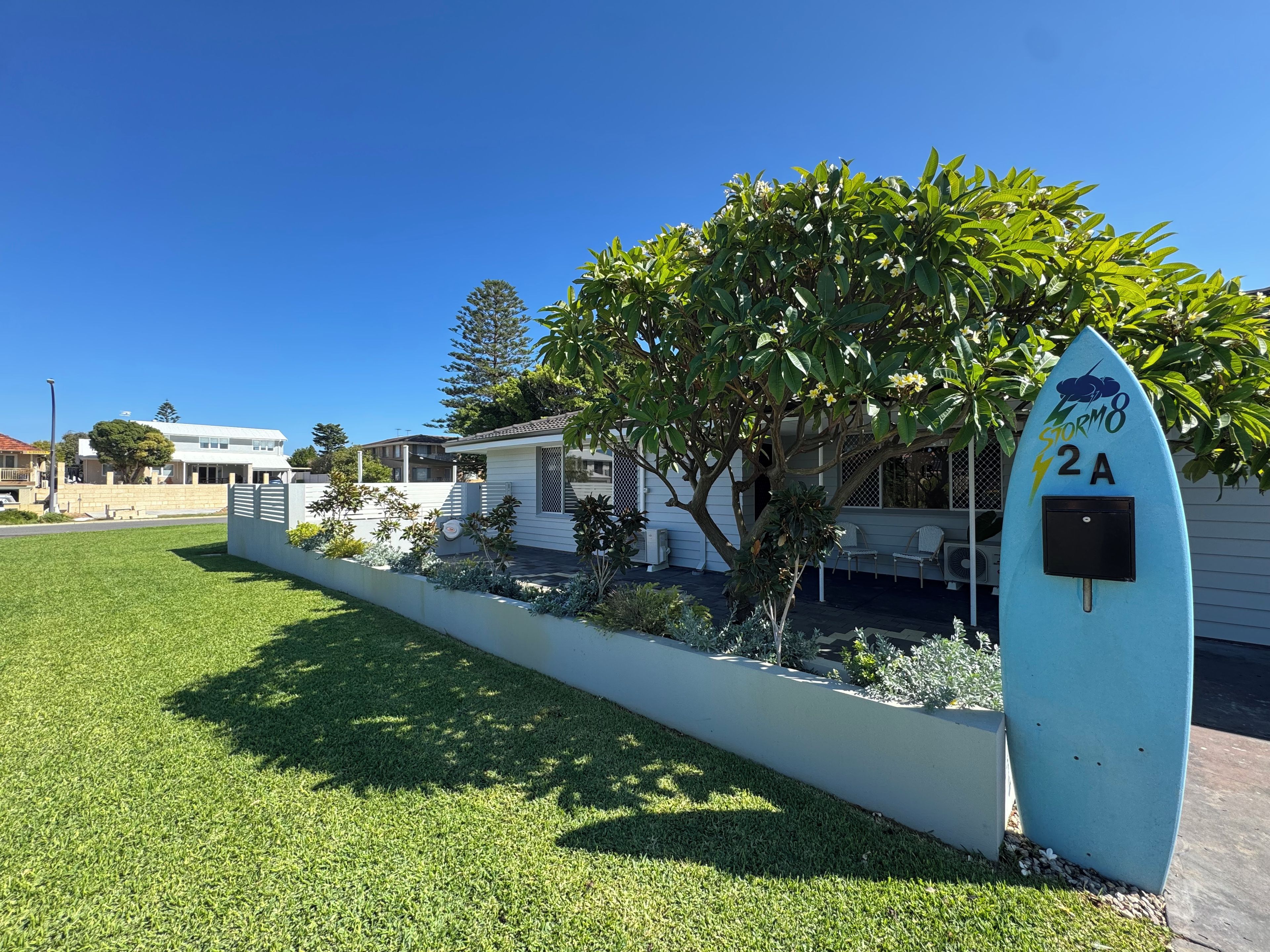 Un quartier résidentiel avec une maison blanche, un arbre et une boîte aux lettres en forme de planche de surf.