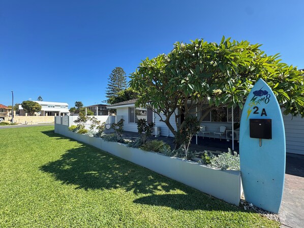A residential area with a white house, a tree, and a surfboard-shaped mailbox.