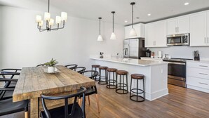 Cozinha moderna com armários brancos, eletrodomésticos de aço inoxidável e uma mesa de jantar de madeira com banquetas.