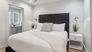 Um quarto moderno com uma cama grande, um ventilador de teto, mesas de cabeceira com luminárias e um espelho sobre a cômoda.