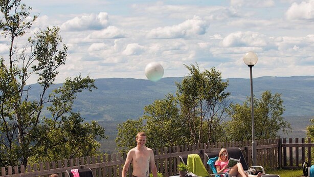 Ein Poolbereich mit Blick auf Berge im Hintergrund, umgeben von Liegestühlen und einem Holzzaun.