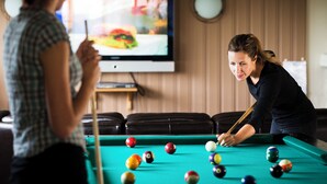 Ein Billardtisch mit Kugeln und ein Fernseher im Hintergrund.