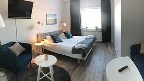 Ein Hotelzimmer mit einem Bett, einem blauen Sessel, einem weißen Tisch und einem dunklen Sofa.