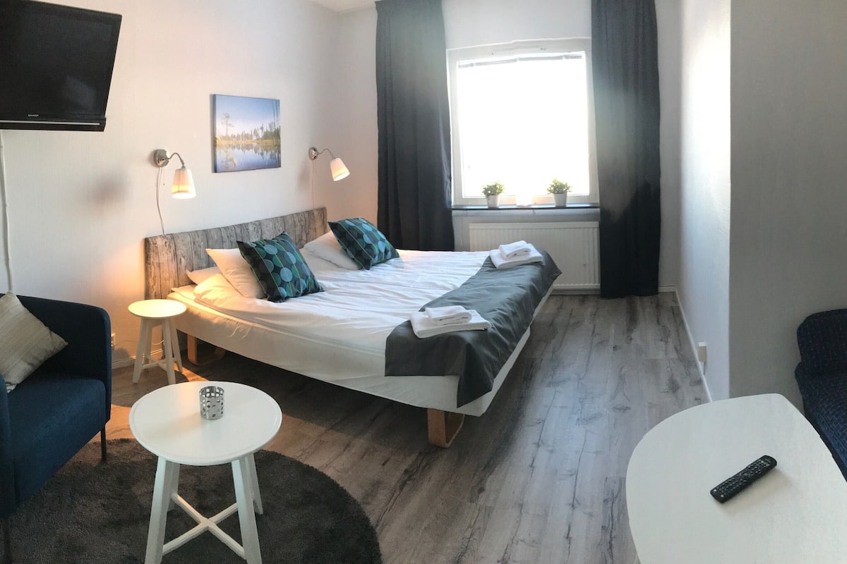 Una habitación de hotel con una cama, un sillón azul, una mesa blanca y un sofá oscuro.