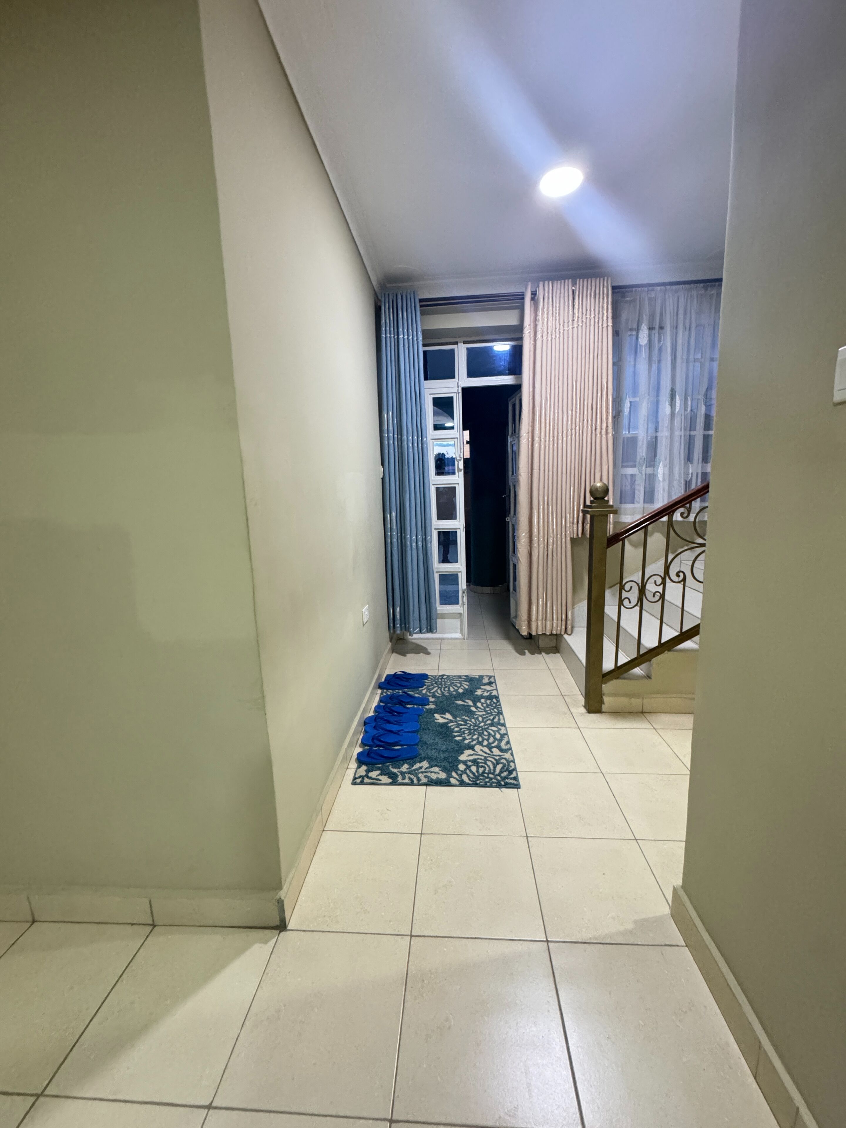 A hallway with a tiled floor, a blue patterned rug, and a staircase with a metal railing.