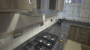 Una cucina con piano cottura a gas, ripiani in granito, mobili in legno ed uno scaffale in vetro.