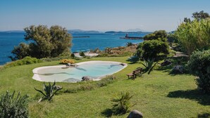Une piscine entourée d’une zone herbeuse, avec des arbres, et offrant une vue sur la mer.