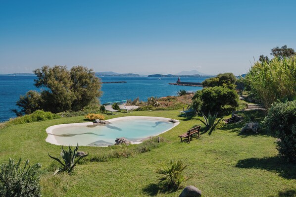 A pool surrounded by a grassy area with trees and a view of the sea.