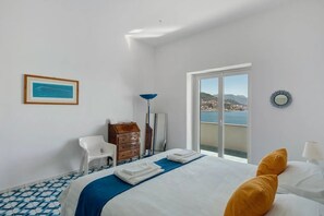 Une chambre d’hôtel avec un lit, un bureau, une chaise, une commode, une lampe sur pied et une vue sur la mer.