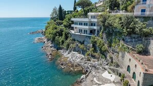 A coastal property with a stone staircase leading to a building, a clear view of the sea, and lush greenery.