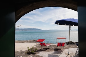 Une vue sur la plage, avec un ciel dégagé, une mer calme et deux chaises de plage rouges et blanches sous un parasol bleu.