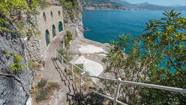 A coastal view with a stone staircase leading down to a beach, overlooking the sea and distant mountains.