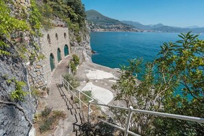 A coastal view with a stone staircase leading down to a beach, overlooking the sea and distant mountains.