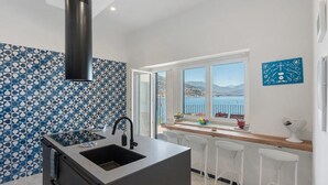 A kitchen with a large window, a sink, and a view of the sea.