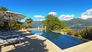 Una piscina con sillas de descanso y una sombrilla, rodeada de vegetación y montañas al fondo.