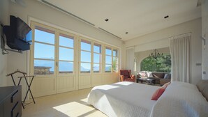 Un dormitorio espacioso con una cama grande, un televisor montado en la pared y vistas a la montaña a través de ventanas amplias.