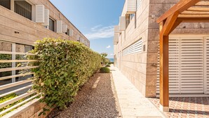 Un sendero estrecho bordeado por edificios con contraventanas de madera, un camino de grava y una estructura de pérgola de madera.