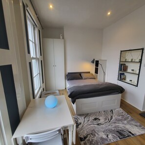 Cozy retreat with a neatly made bed, bedside table, and desk, set against a simple white backdrop.