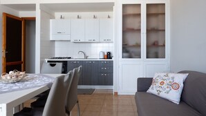 A compact living space with a kitchenette, a dining area, and a sofa with a patterned pillow. - Apple House (Giardini Naxos)