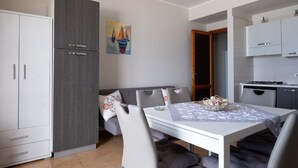 A compact kitchen with a dining area, grey cabinets, a painting, and a small dining table with chairs. - Apple House (Giardini Naxos)