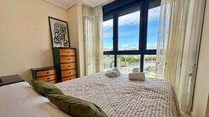 Un dormitorio con cama, cómoda, ventana con cortinas y vista al exterior.