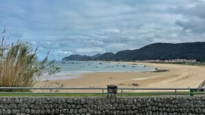 Una playa costera con un muro de piedra en primer plano y una montaña al fondo.