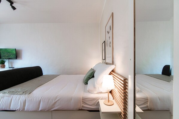 A modern bedroom with a bed, bedside table, and a television on a stand.