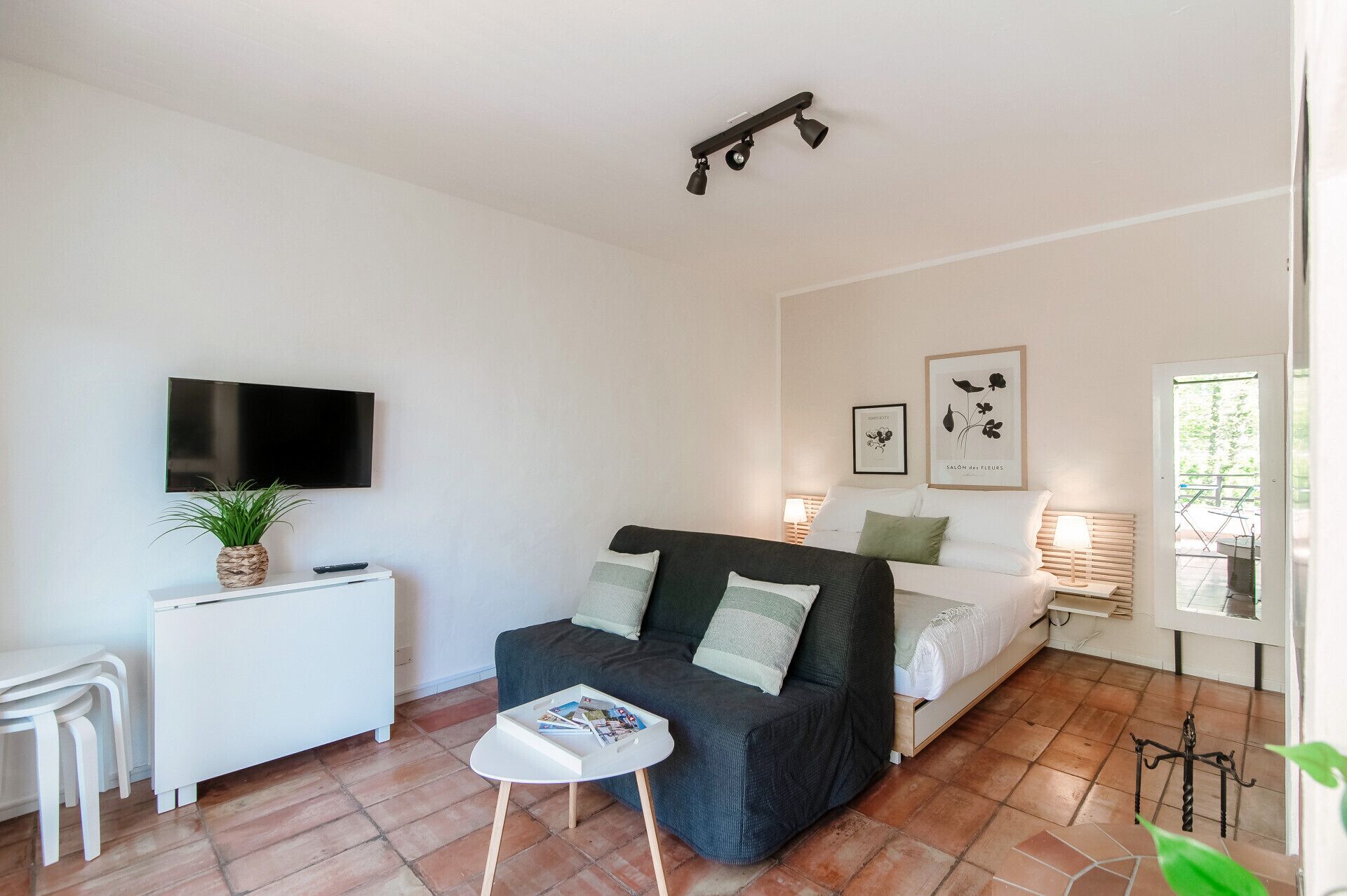 A modern bedroom with a bed, a TV, a small table, and a potted plant.