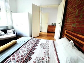 A bedroom with a bed, a wooden headboard, a window, and a brick wall. - Apartment in Historic Building - Sleeps 4 (Timisoara)