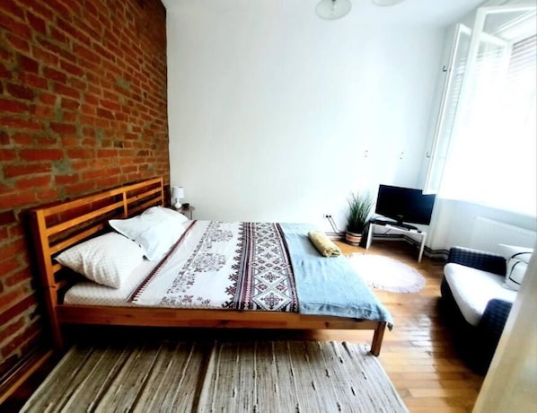 A bedroom with a wooden bed, a TV, and a window. - Apartment in Historic Building - Sleeps 4 (Timisoara)