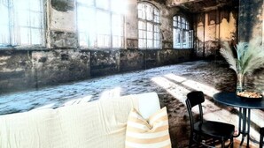 Ein Zimmer mit großen Bogenfenstern, einem kleinen runden Tisch mit Stühlen und einer Topfpflanze.