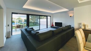 Una sala de estar moderna con un sofá seccional negro, un televisor de pantalla plana y una puerta de vidrio que da a un patio con piscina.