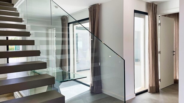 Un interior moderno con una escalera de cristal, una puerta que da a una habitación luminosa y vistas a través del vidrio.