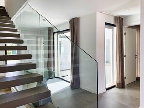 A modern interior with a glass staircase, a door leading to a bright room, and a view through the glass. - Modern villa with heated pool. Vibrant Vilamoura is within walking distance. (Quarteira)