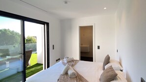 Un dormitorio moderno con una cama grande, vista a un césped verde y una puerta de vidrio que da al exterior.