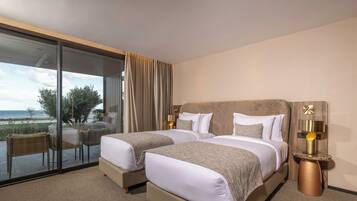 A hotel room with two beds, a glass door leading to a balcony, and a small table with a lamp.