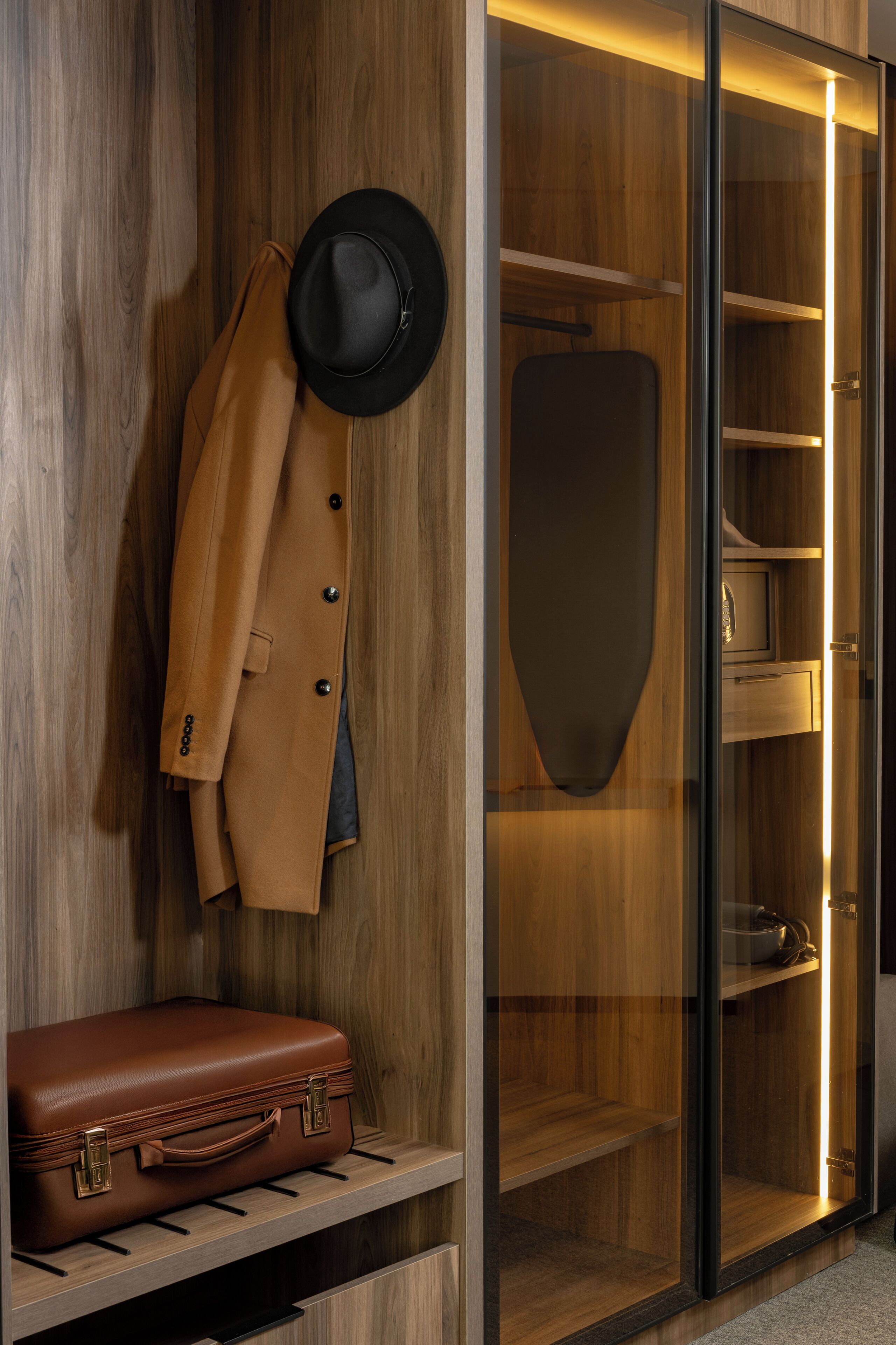 Un armadio in legno con cappotto appeso, un cappello e una valigia.