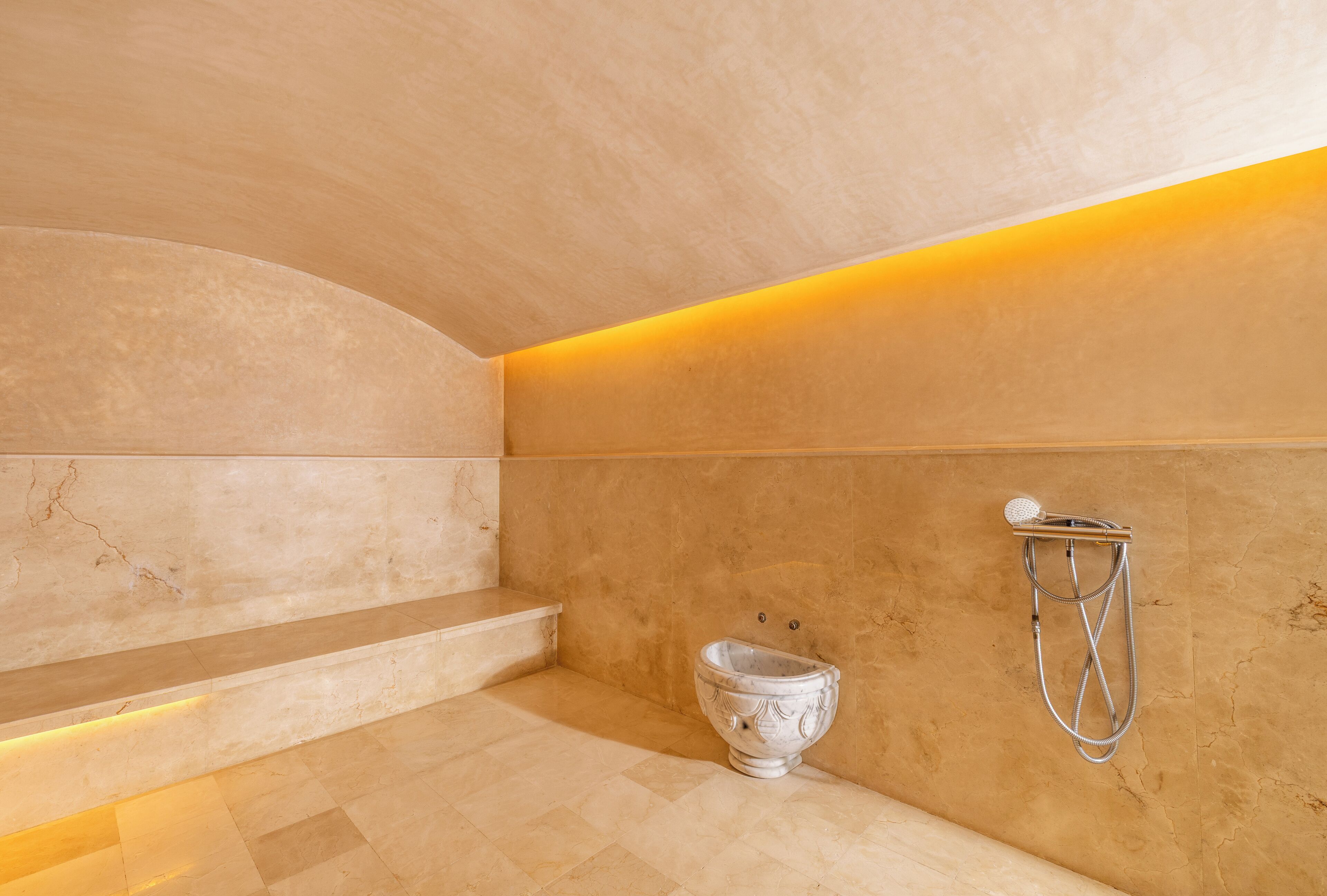 A modern bathroom with a marble floor, a built-in bench, and a wall-mounted shower.