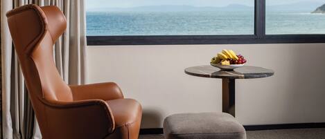 Habitación moderna con un sillón de cuero, una pequeña mesa redonda con fruta y vistas al mar.