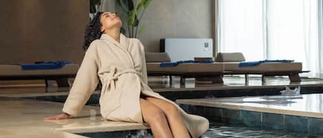 A person sitting in a bathtub in a modern room with a massage chair and a large window.