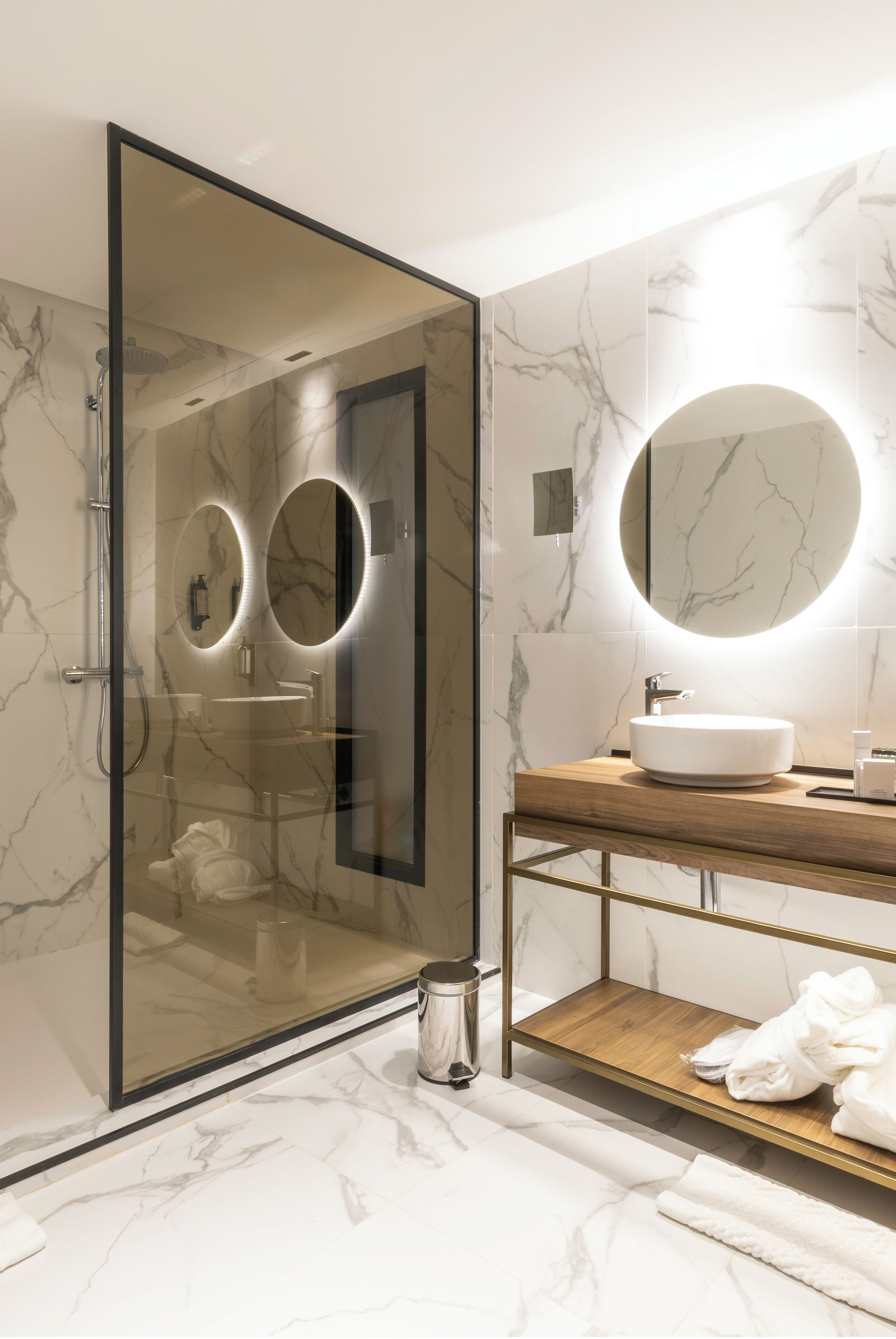 A modern bathroom with a glass-enclosed shower, a round mirror, and a wooden vanity with a sink.