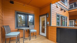 A wooden deck with a table and two chairs, a sliding glass door, and a balcony with a railing. - Pet Friendly Condo, Suncadia Pool Access (Cle Elum)